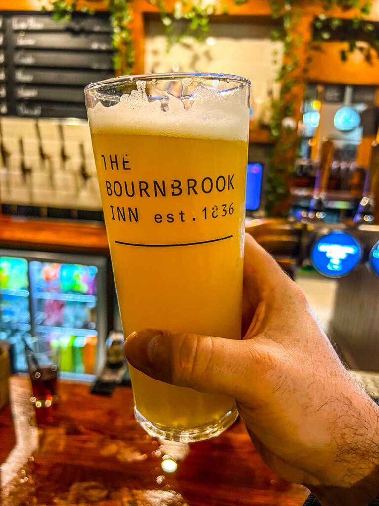 Hand holding a pint of real ale at the bar with the words 'The Bournebrook Inn est 1836' written on the glass