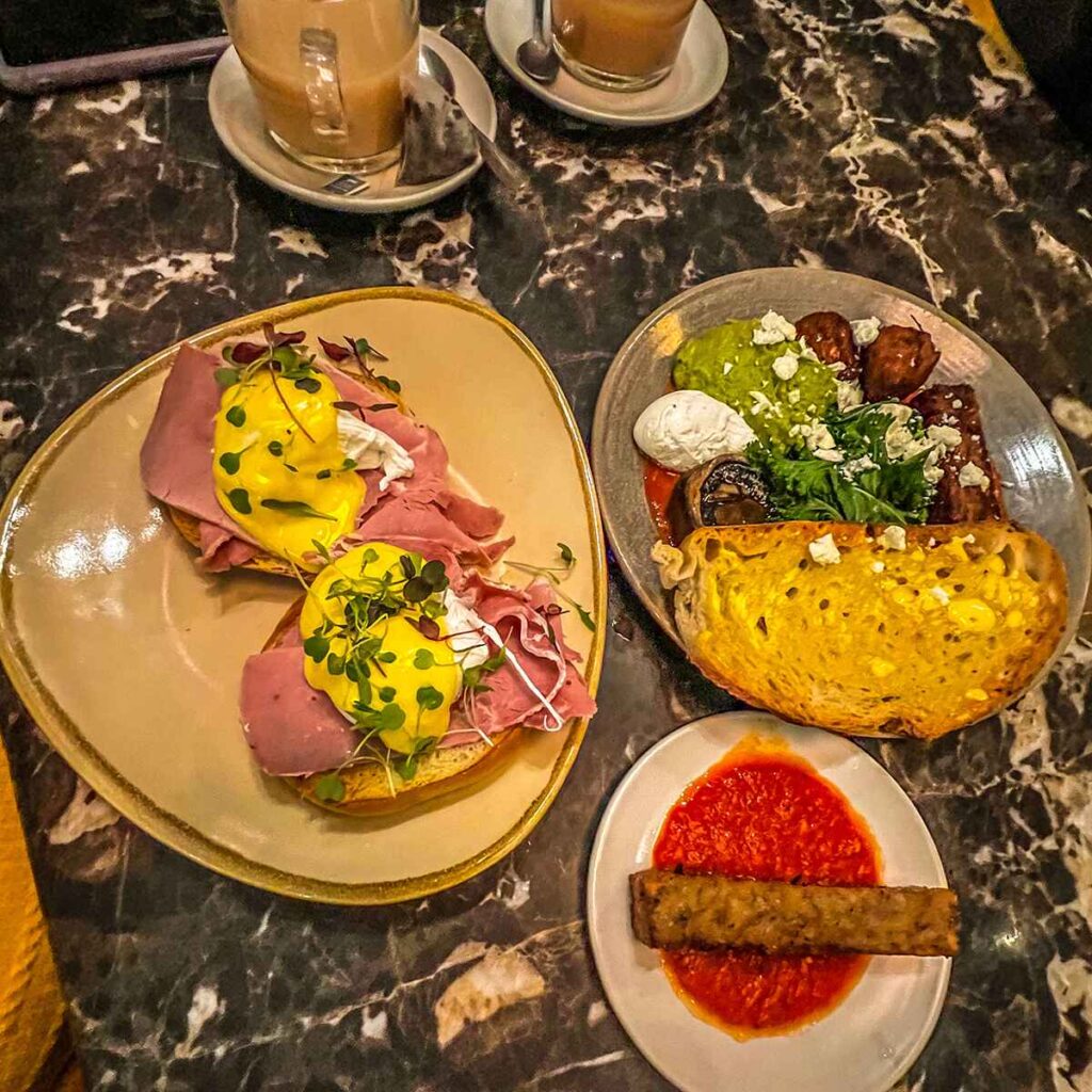 Three plates of brunch foods, eggs, ham, hollandaise, toast and two coffees