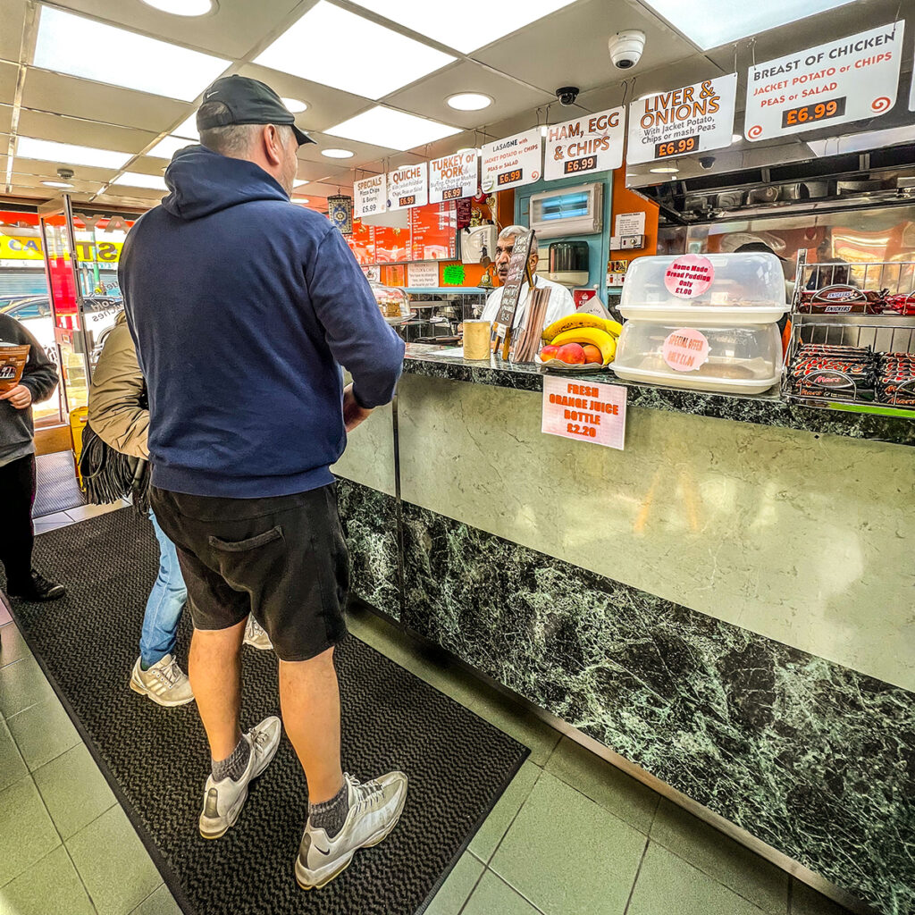 A man in shorts and hoody stands at the counter at the Clock cafe, Northfield. 