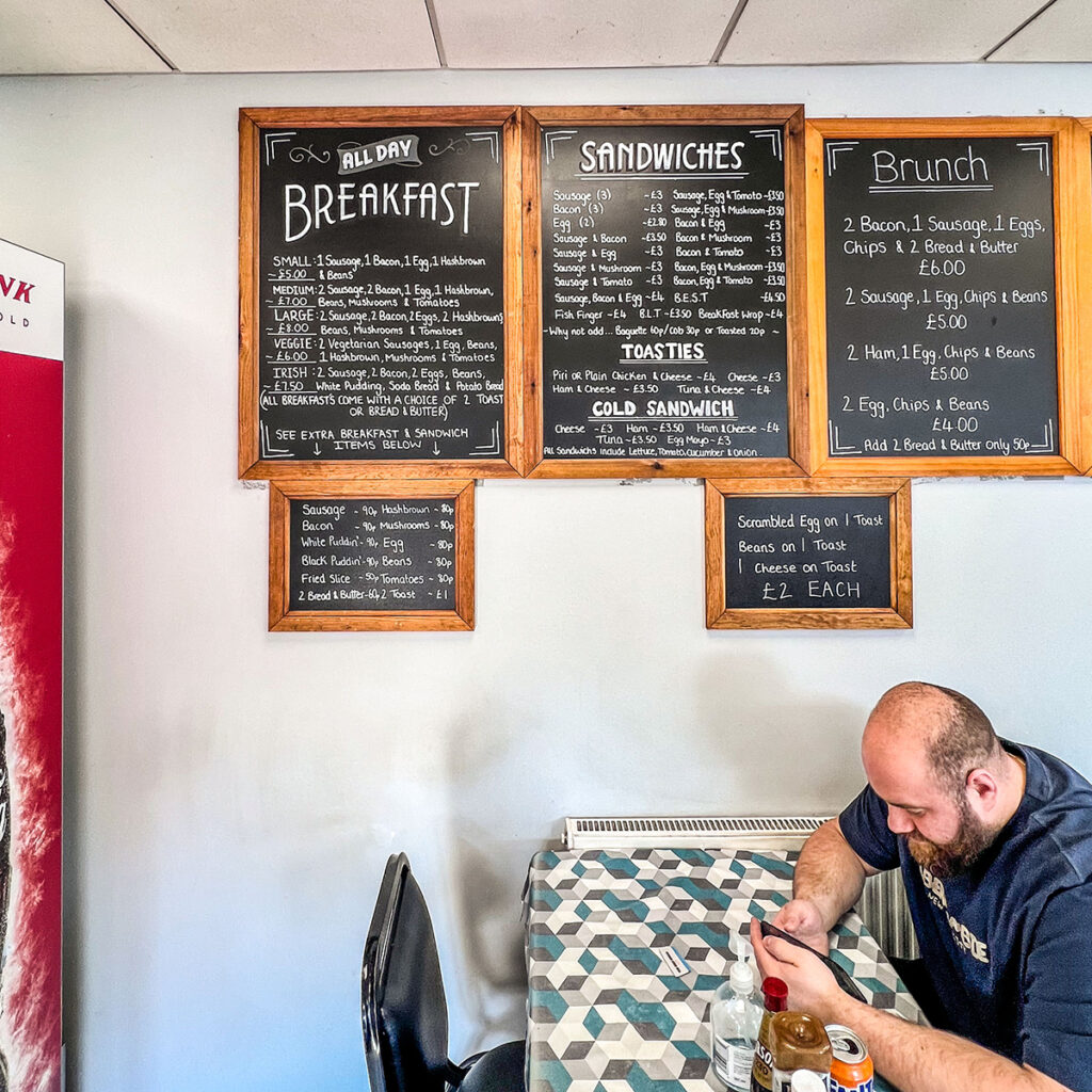 An internal shot of Tyseley Corner Cafe. A person is sat at the table using their mobile phone