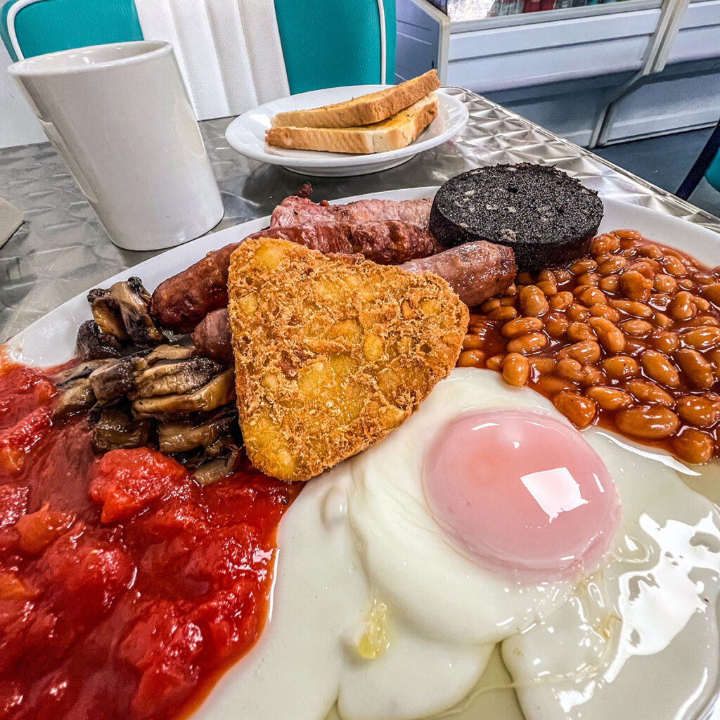 A huge full English breakfast at Billsedge Cafe, containing fried egg, tomatoes, has bacon, black pudding, beans, mushrooms, toast and a mug of tea.

